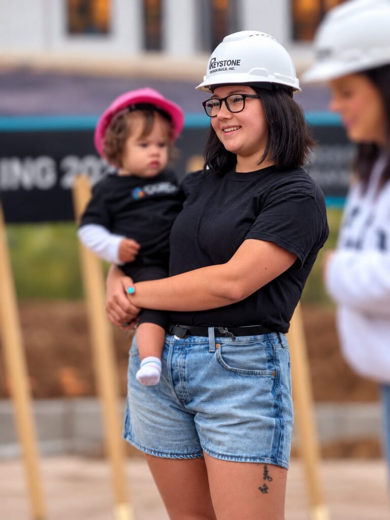 A team member holding a child in a hard hat at the groundbreaking