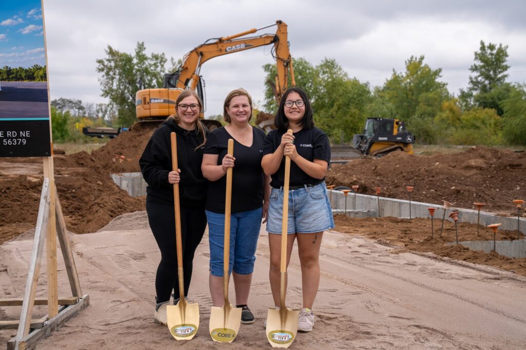 Three team members with gold shovels in front of the excavator